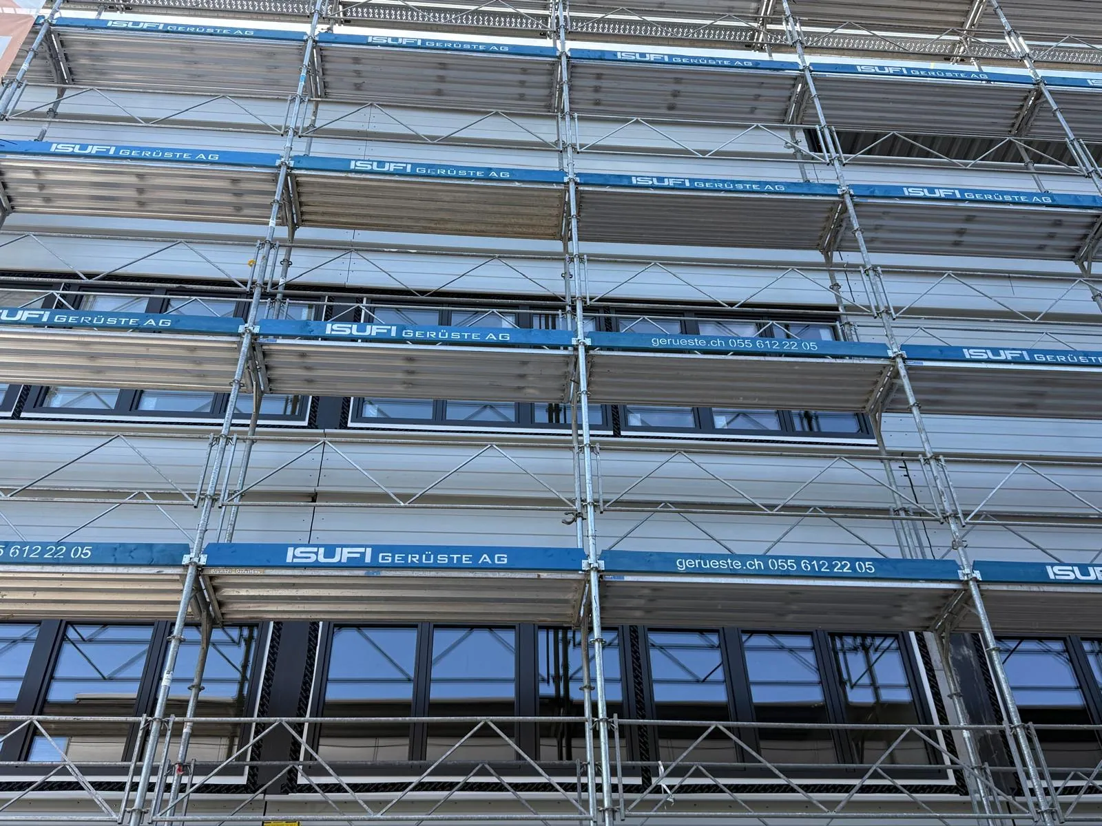Fassadengerüst vor einer Fensterfront Fassadengerüst vor einer Fensterfront. Arbeitsbühnen auf mehreren Ebenen ermöglichen Arbeiten an der verglasten Gebäudefassade. Referenzfoto der Isufi Gerüste AG.