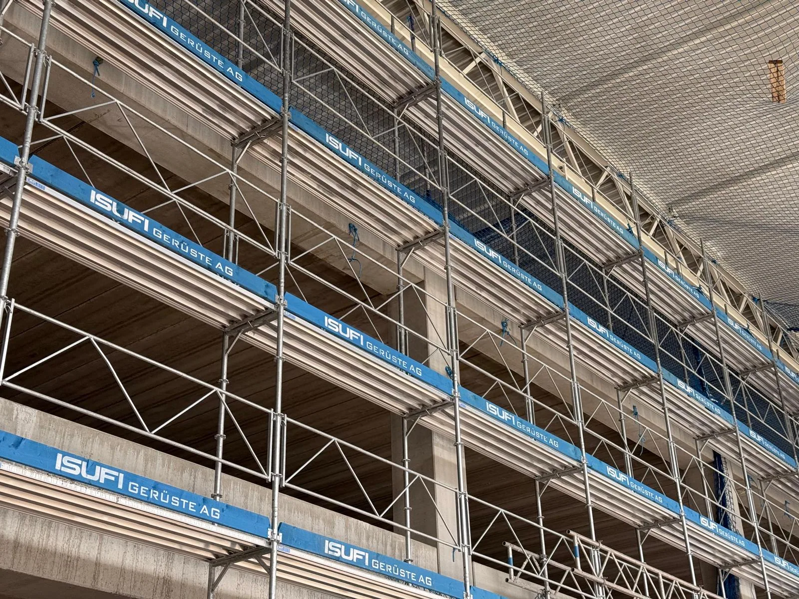 Fassadengerüst mit mehreren Arbeitslagen Fassadengerüst mit mehreren Arbeitslagen. Mehrere übereinanderliegende Gerüstebenen schaffen gut erreichbare Arbeitsbereiche für Fassadenarbeiten am Gebäude. Referenzfoto der Isufi Gerüste AG.