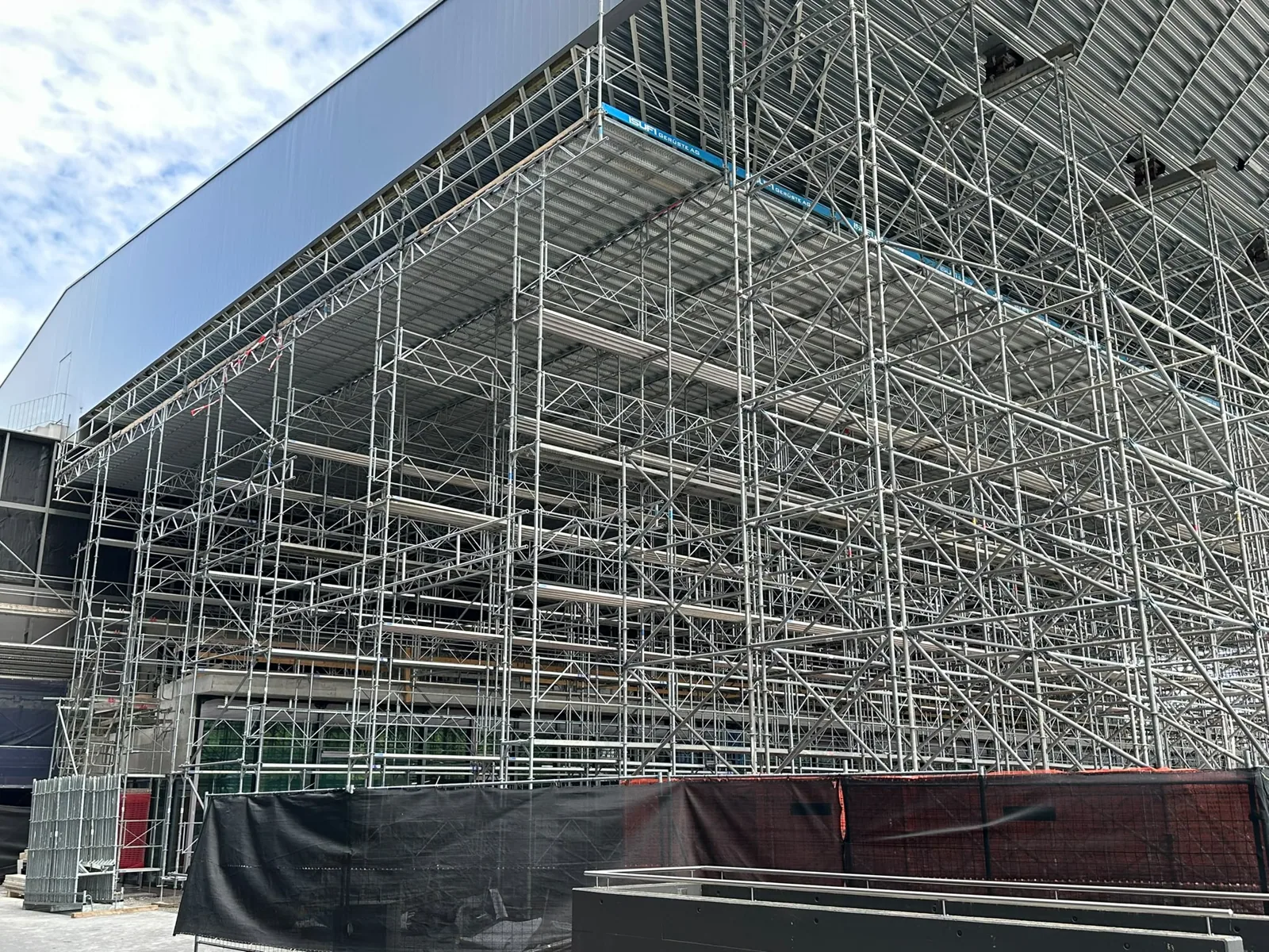 Flächengerüst in einer grossen Halle Flächengerüst in einer grossen Halle. Ein weitläufiges Arbeitsgerüst zwischen den Stahlträgern bietet Zugang für Arbeiten im oberen Hallenbereich. Referenzfoto der Isufi Gerüste AG.