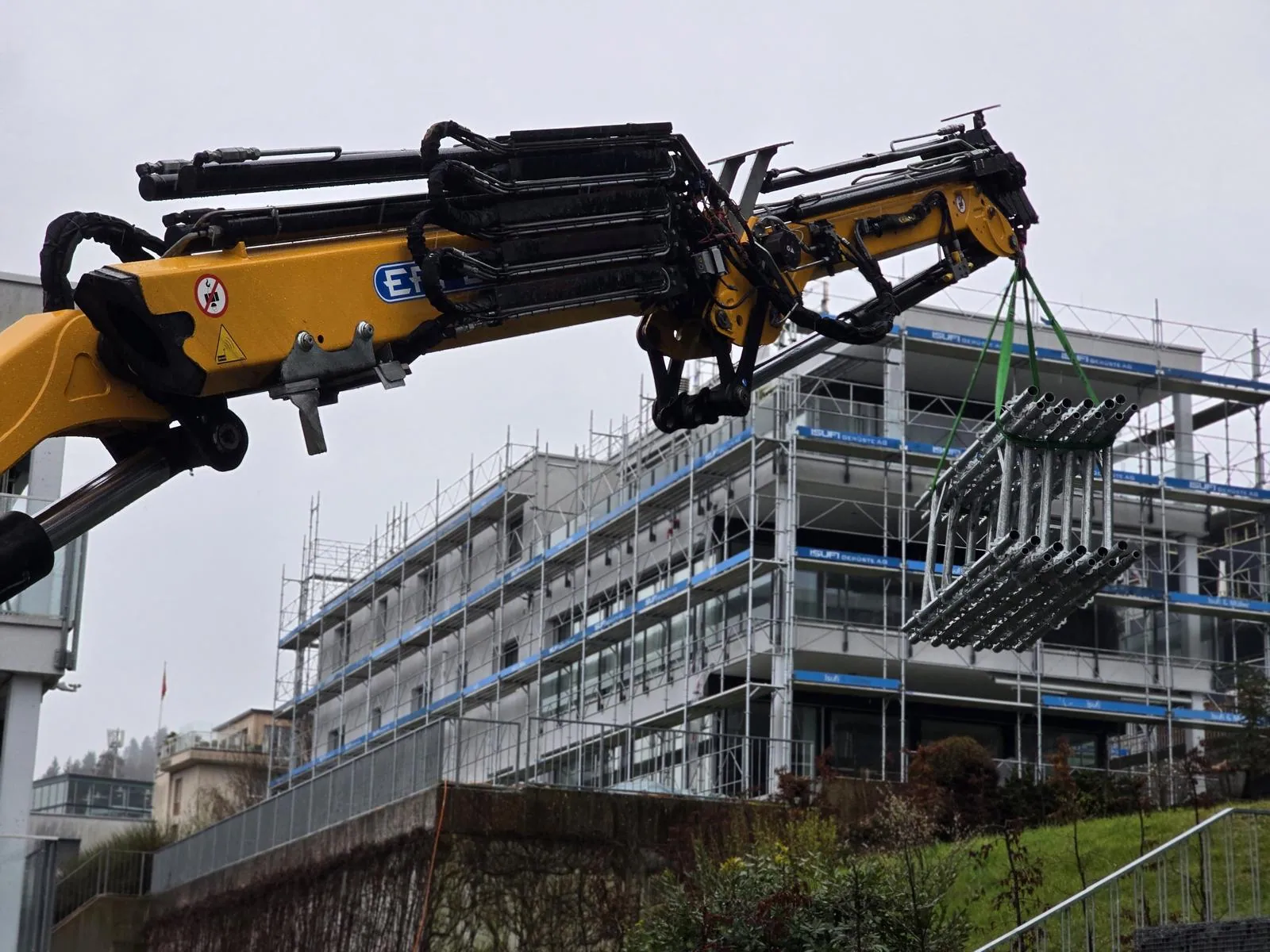 Gerüstmaterialtransport mit dem Baustellenkran Gerüstmaterialtransport mit dem Baustellenkran. Gebündeltes Gerüstmaterial wird mit dem Kran für die Montage auf der Baustelle bereitgestellt. Referenzfoto der Isufi Gerüste AG.